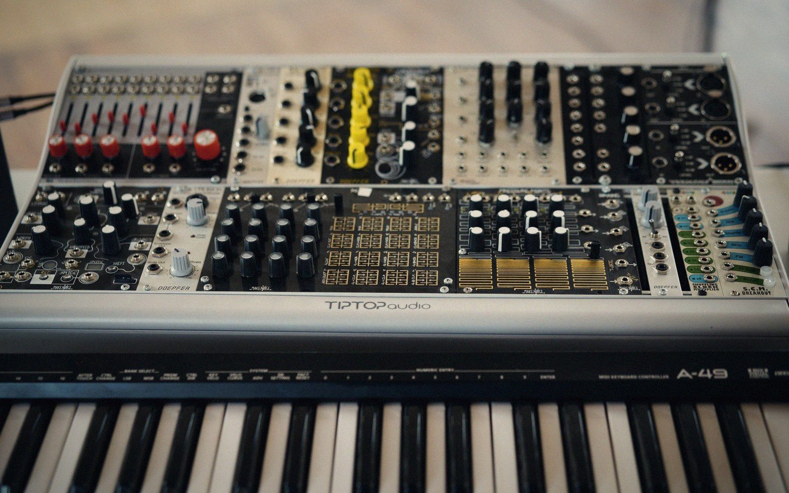 Wide shot of a fully patched case with dense cable routing — orange, grey and white cables layered across the module faces, lit by a single overhead lamp
