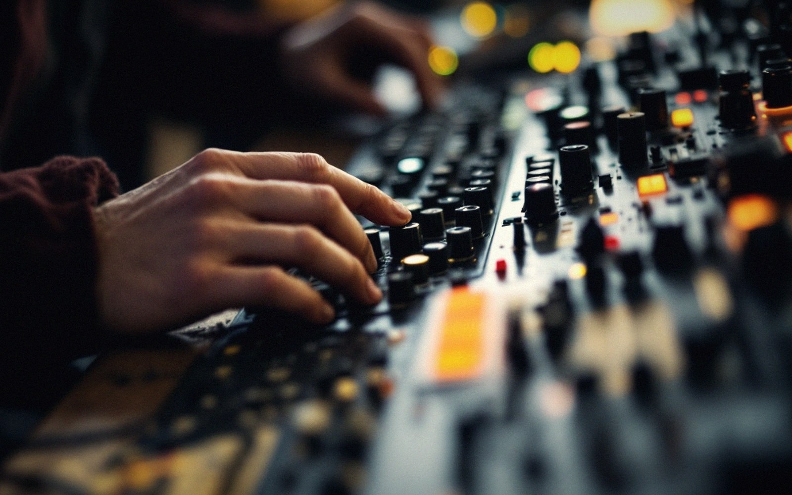 Hands adjusting knobs on a mixing console covered in illuminated buttons and sliders