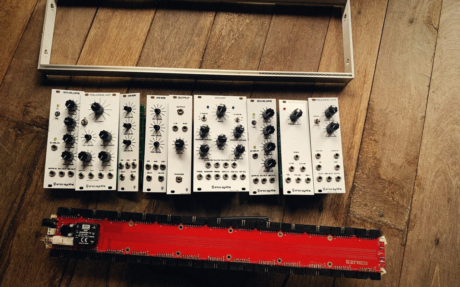 Eurorack synthesizer modules with knobs laid out above a red power bus board