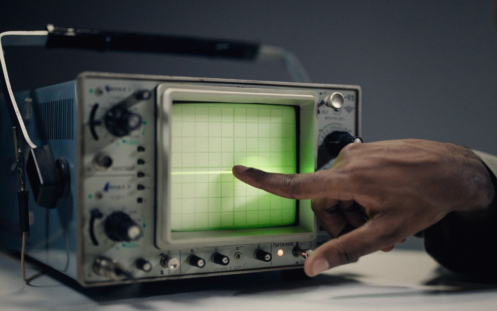 A finger points at a green waveform on a vintage oscilloscope screen