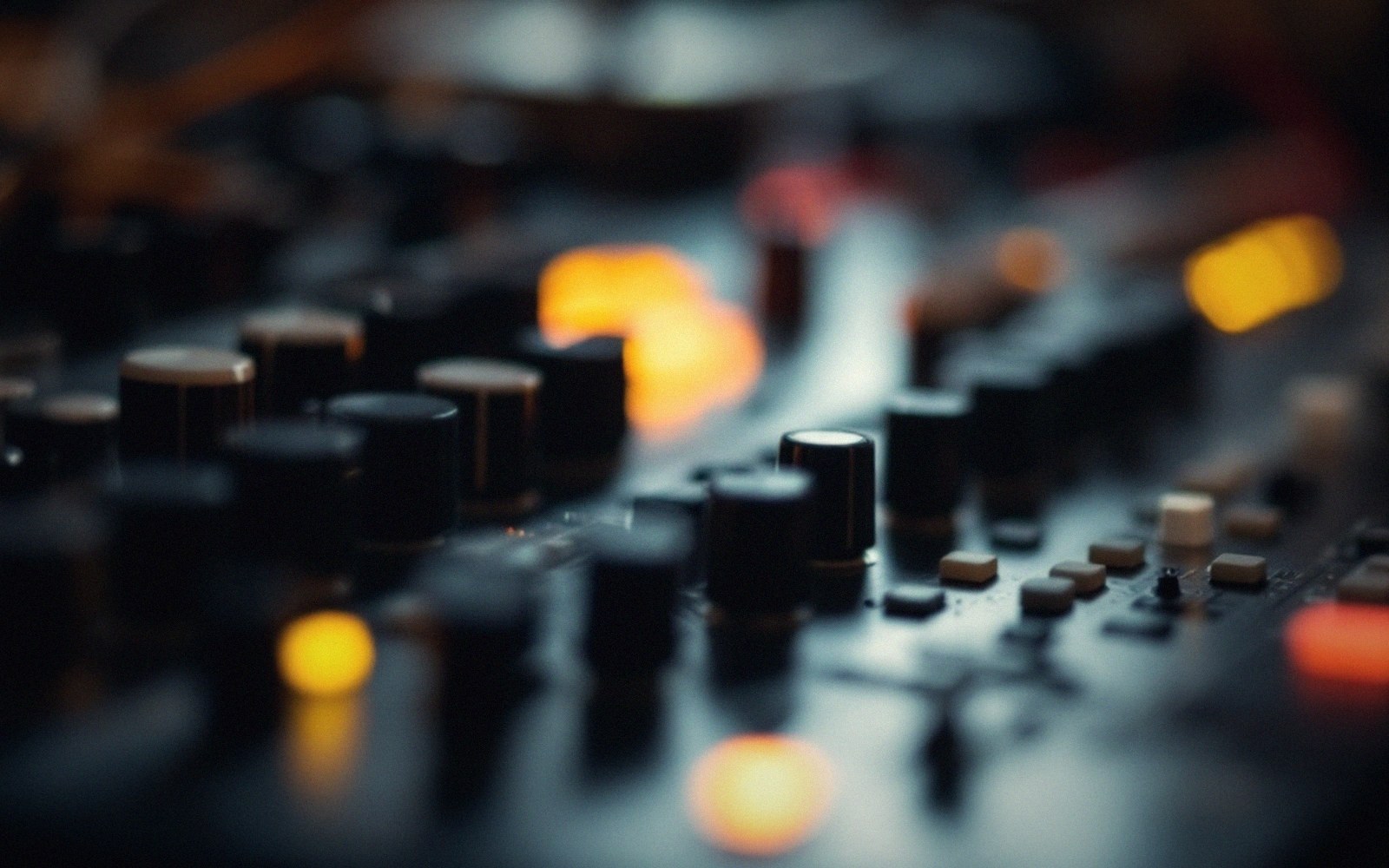 Close-up of knobs and buttons on a mixing console with blurred amber lights